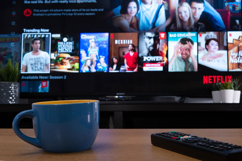 Hình ảnh website của Netflix được hiện ra trên ti vi, có cốc nước và điều khiển nằm trên bàn