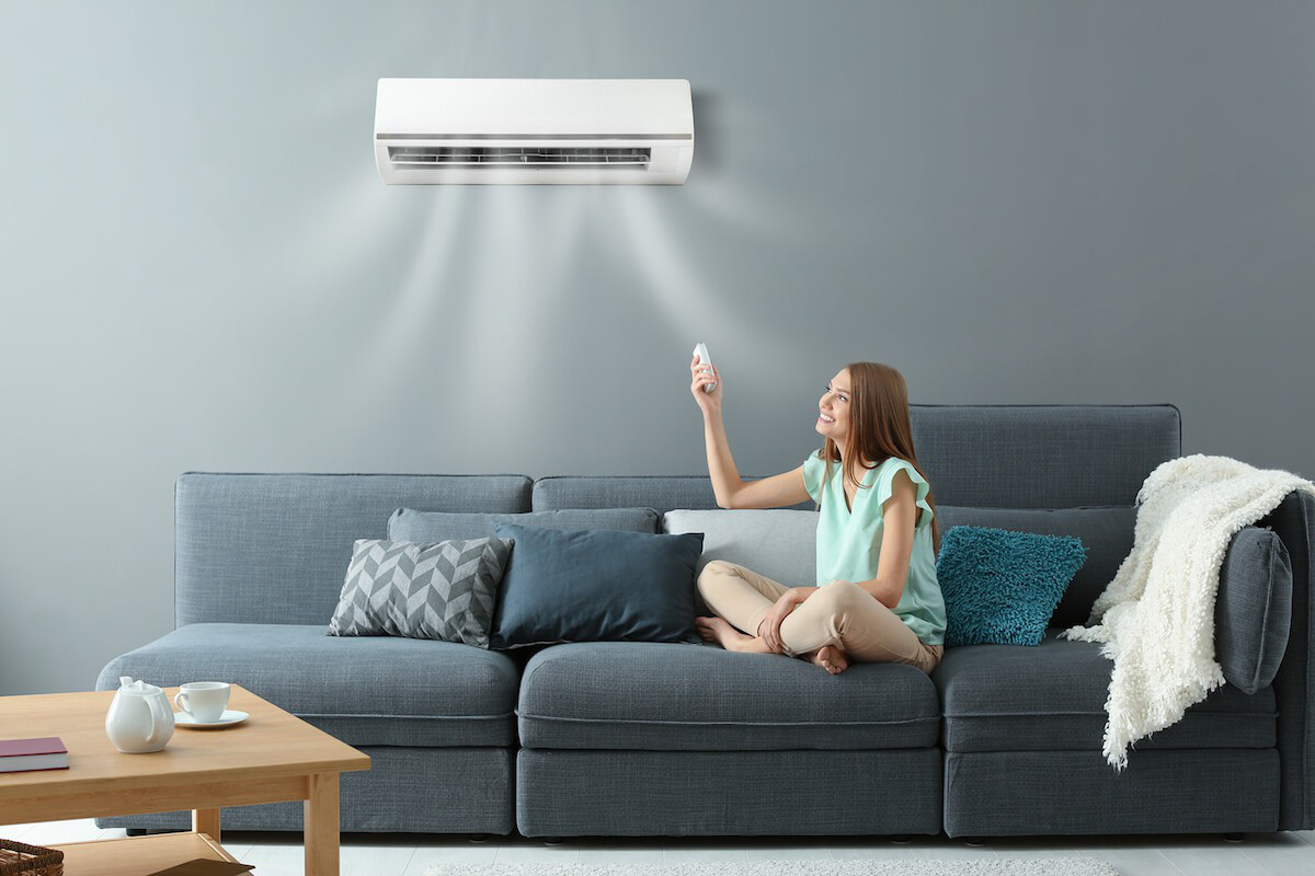 Cô gái đang ngồi trên ghế sofa đang sử dụng remote để chỉnh máy lạnh.