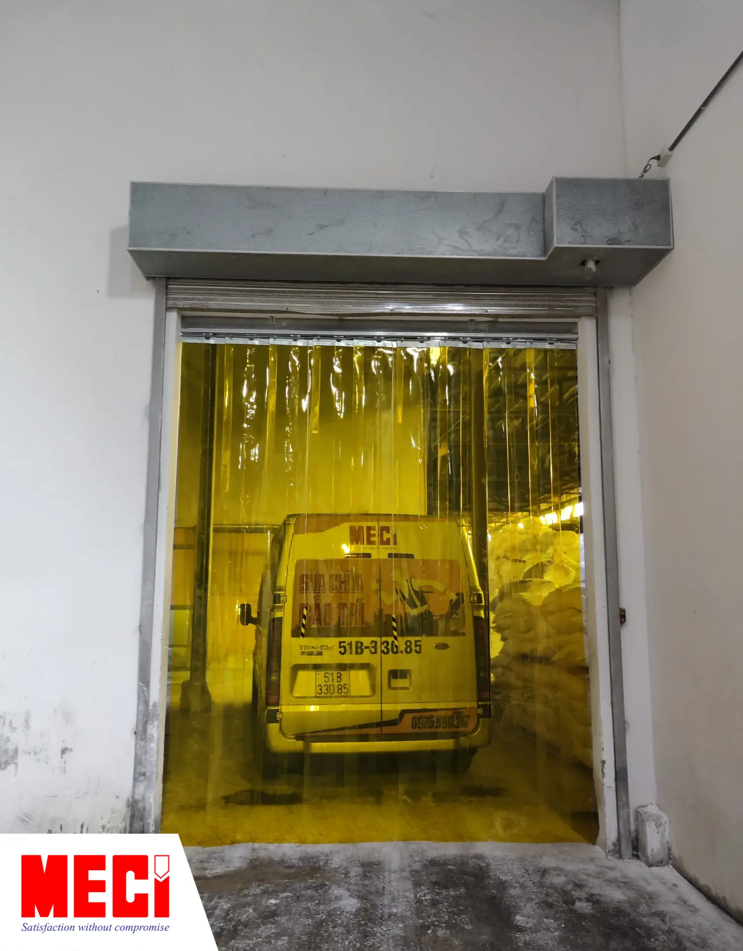 rèm nhựa pvc hệ xếp xoay màu vàng được lắp ở lối ra vào một nhà kho, phía trong có xe bán tải mang logo MECI