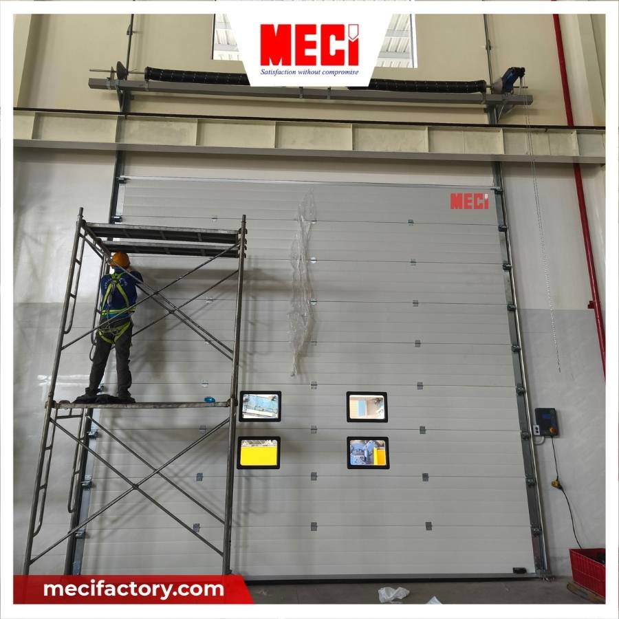 Kỹ thuật MECI đang đứng trên giàn giáo để lắp đặt cửa trượt trần thẳng đứng